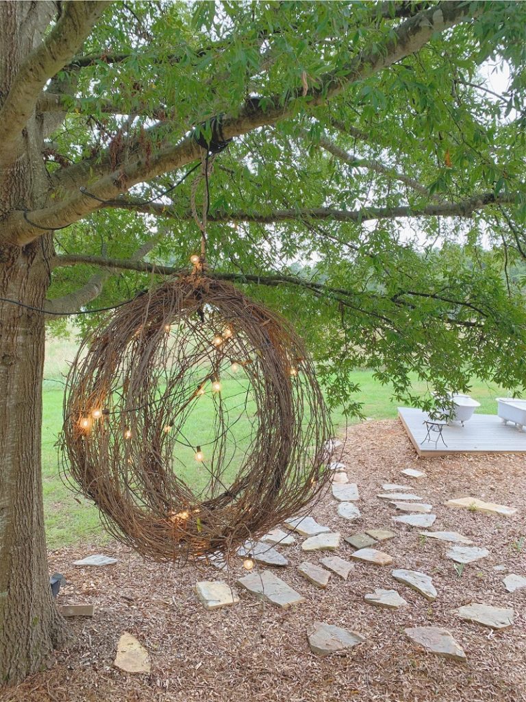photo of a string light lit twig ball hanging from a tree branch